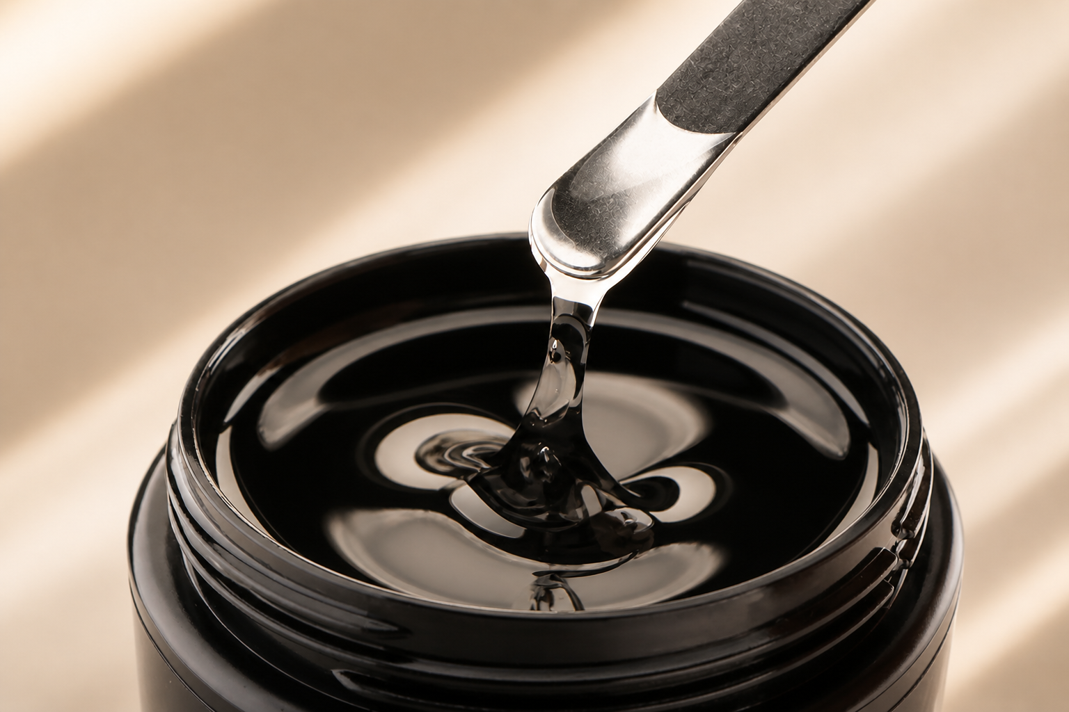 Clear builder gel forming a controlled ribbon from a metal spatula above the jar